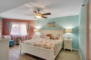 A bedroom with a bed, two bedside tables with lamps, a ceiling fan, a window with curtains, and a chair.
