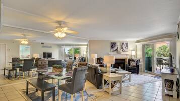 A spacious living area with a dining table, comfortable seating, a fireplace, and large windows offering a view of the outdoors.