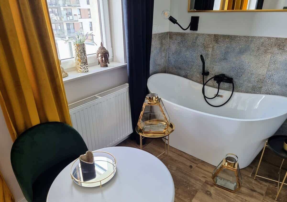 A modern bathroom with a freestanding bathtub, a small round table with a decorative item, and a window with curtains.
