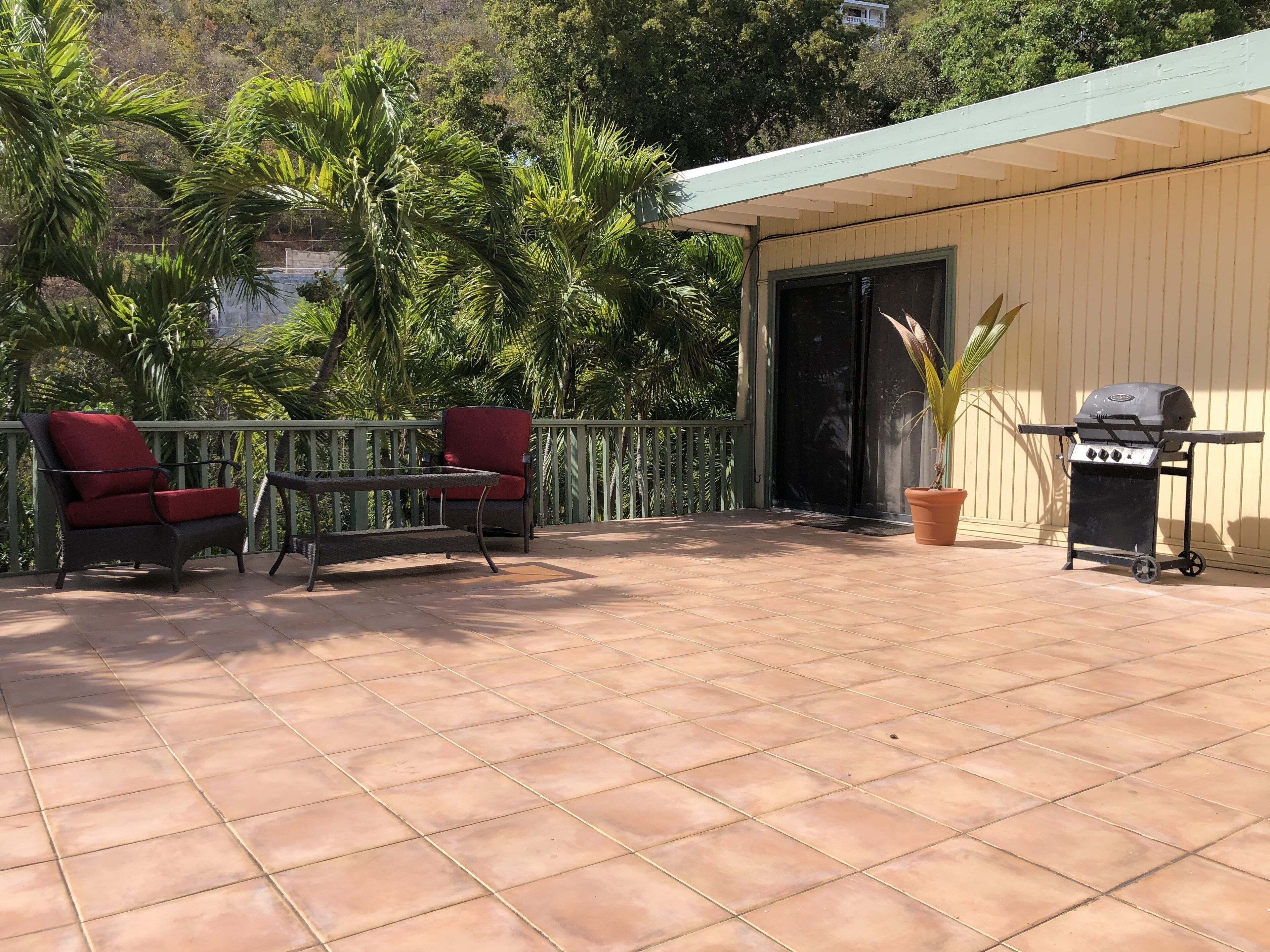 Une terrasse avec un sol carrelé, deux chaises rouges, une petite table, un barbecue et une plante en pot.
