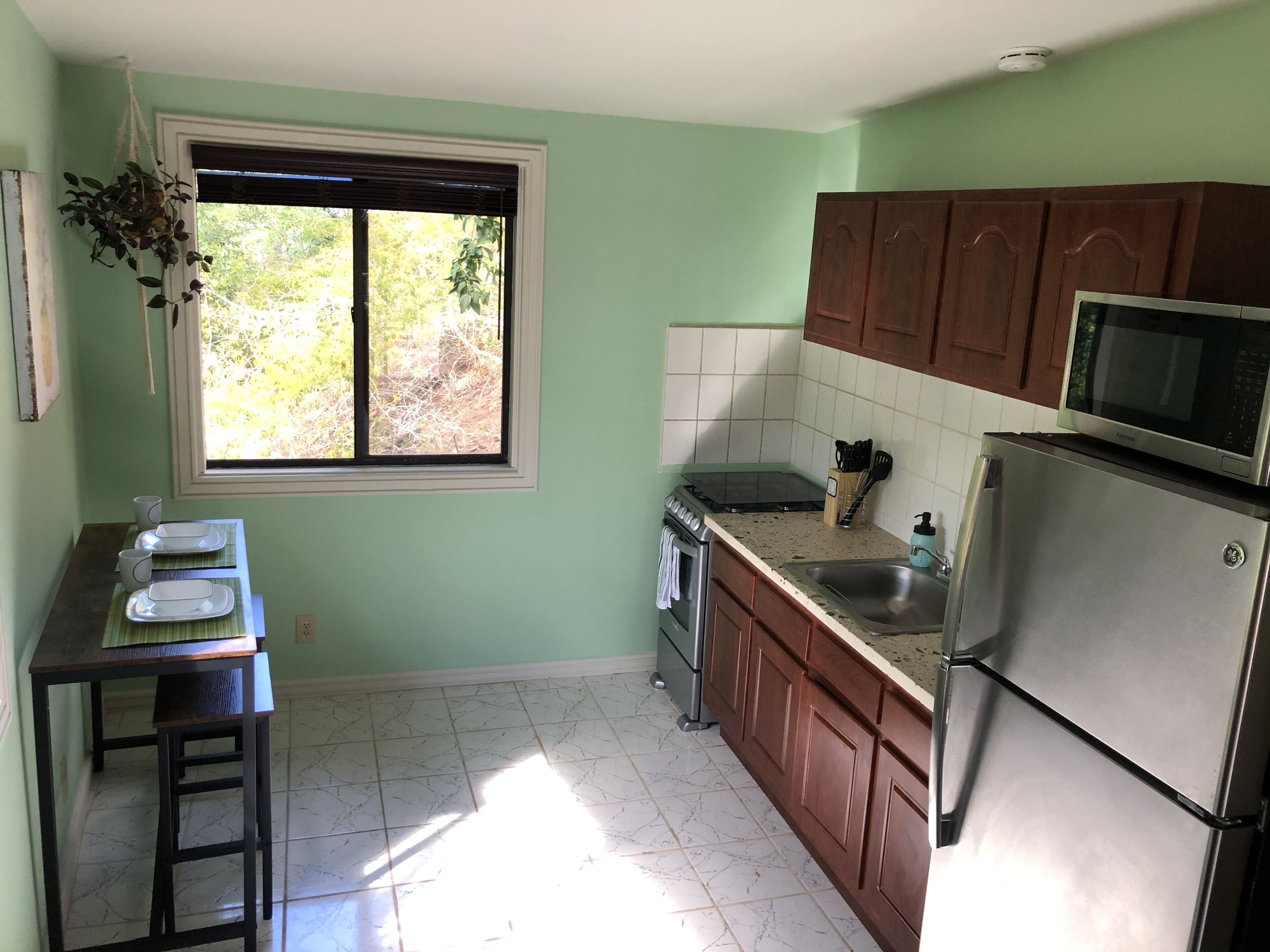 A kitchen with a window, a microwave, a refrigerator, and wooden cabinets.