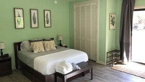 A bedroom with a bed, bedside tables, a bench, a ceiling fan, a wardrobe, and a window with curtains. - Darling Palms Tree House: Beachside Studio Oasis (St Thomas)