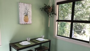 A room with a green wall, a window with blinds, a pineapple artwork, and a hanging plant. - Darling Palms Tree House: Beachside Studio Oasis (St Thomas)
