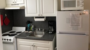 Una cucina compatta con mobili bianchi, un fornello, un forno a microonde e un frigorifero.