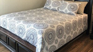 Un letto rifatto con una coperta a motivi e cuscini, una testiera in legno scuro e un pavimento in legno.
