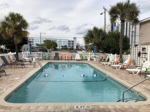 Une piscine rectangulaire à l’eau d’un bleu cristallin, entourée de chaises longues et d’une clôture blanche en bois.