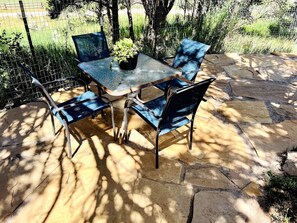 Een terras met een tafel met glazen blad en vier stoelen, omringd door stenen vloer en een gaashek.