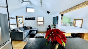 A modern living room with a sofa, a coffee table, and a TV. There is a bed with a green wall and a window.