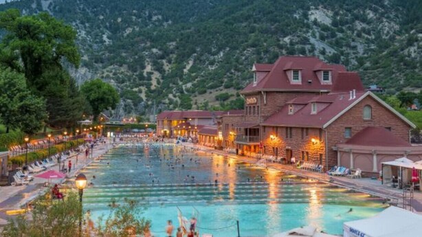 A swimming pool area with a building adjacent to it, surrounded by trees and hills.