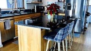 A modern kitchen with a central island, bar stools, stainless steel appliances, and a clock on the wall.