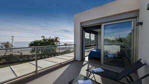 A balcony with a glass door, a bed, and a view of the beach and ocean.