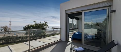 Un balcón con puerta de cristal, una cama y vista a la playa y al océano.