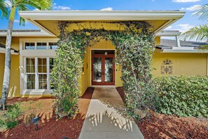 Stunning two-story residence with a charming entrance, surrounded by lush landscaping and a beautiful vine-covered archway.