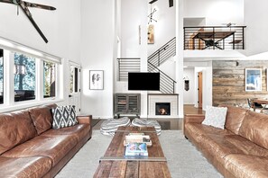 A modern living room with leather sofas, a fireplace, a staircase, and a large TV.