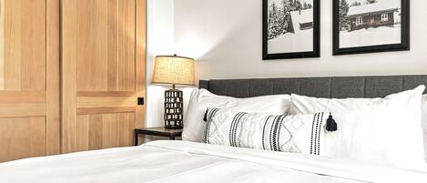 A hotel room with a large wooden wardrobe, a bedside table with a lamp, a bed with white bedding, and two framed pictures on the wall.