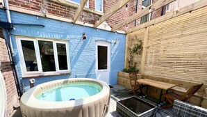 Un jacuzzi en un patio trasero con terraza de madera y mobiliario exterior.