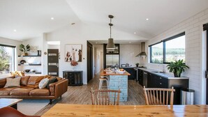 A modern kitchen with a central island, a dining area with a wooden table, and a living room with a brown leather sofa. - Minaret Ridge | Holiday home close to the lake (Wanaka)