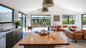 A modern kitchen with a central island, dining area with chairs, and a living room with a sofa. - Minaret Ridge | Holiday home close to the lake (Wanaka)