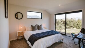 A bedroom with a bed, bedside tables, a mirror, and a view of the outdoors. - Minaret Ridge | Holiday home close to the lake (Wanaka)
