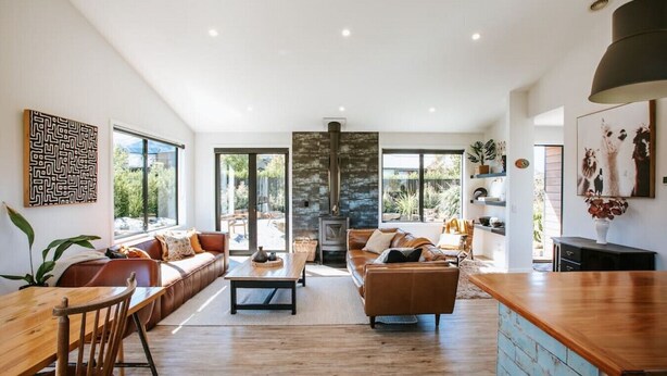 A modern living room with a wooden dining table, leather sofas, and a stone fireplace. - Minaret Ridge | Holiday home close to the lake (Wanaka)
