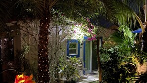 Un jardín bien iluminado con una palmera, distintas plantas y un pequeño espacio de descanso con mesa y sillas.