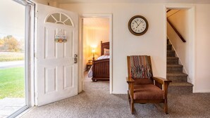 Un couloir avec une chaise en bois, une horloge et un escalier menant à une chambre.