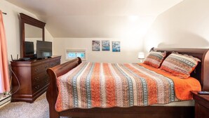 Une chambre à coucher avec un lit, une commode et un grand miroir. Il y a trois tableaux accrochés au mur et une fenêtre avec des stores.