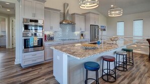 Cozinha moderna com armários brancos, eletrodomésticos de aço inoxidável, uma ilha grande com banquetas e iluminação pendente.