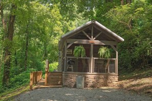 Uma pequena cabana de madeira com base de pedra, um deck de madeira e uma placa com a inscrição 'Lodge'.