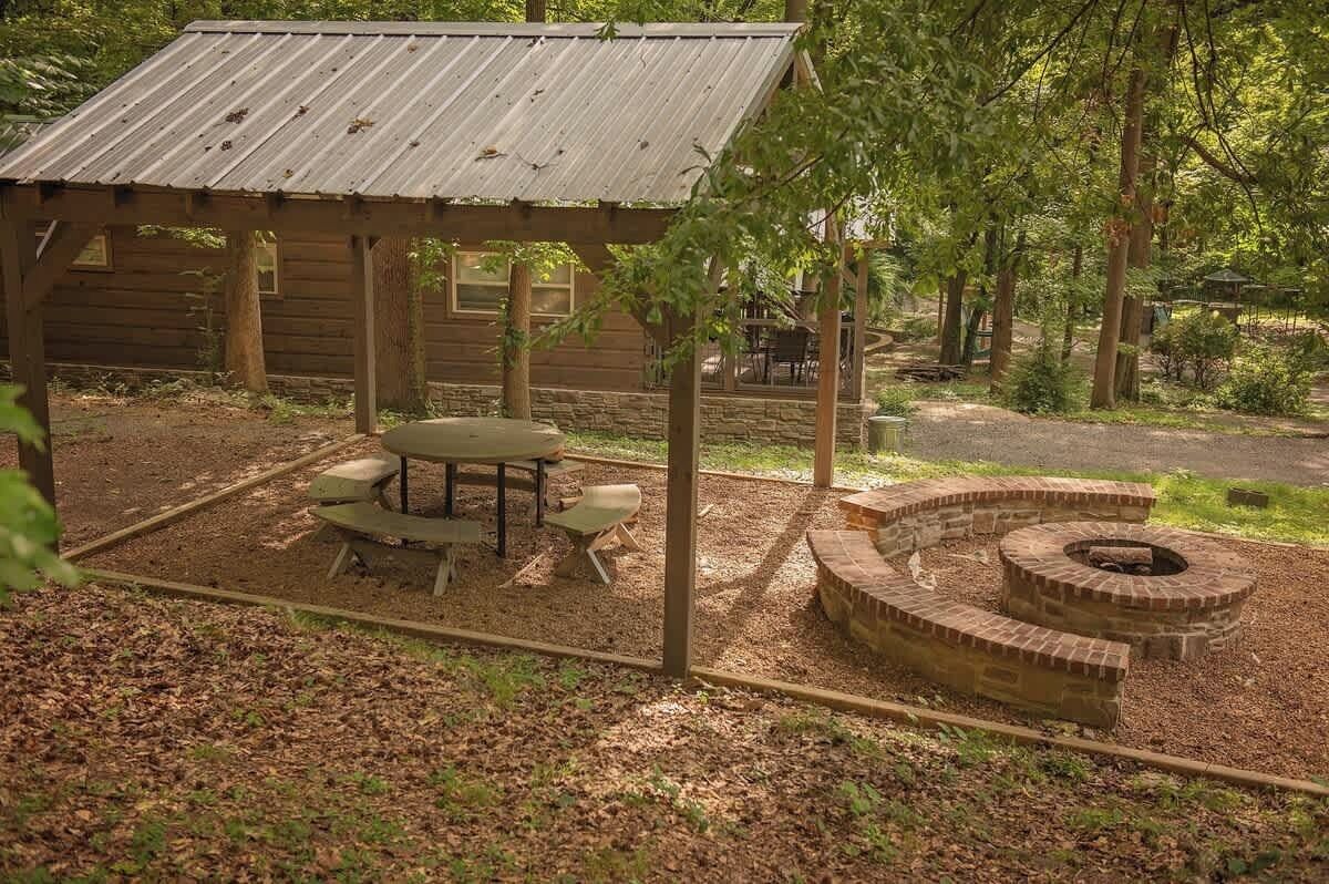Eine rustikale Holzhütte mit überdachter Veranda, einem runden Feuerkorb und einem Picknicktisch.