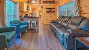 Un intérieur de chalet chaleureux avec un canapé, des fauteuils, une table à manger et un coin cuisine.