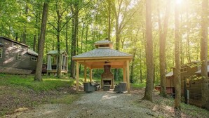 Un chalet rustique doté d’un espace extérieur couvert avec des sièges, d’une cheminée et d’un chemin de gravier menant à l’entrée.