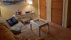 Ein Wohnzimmer mit einer Couch, einem Couchtisch, einer Lampe, einem kleinen Tisch mit Büchern und einer Taschentuchbox, und zwei Türen.