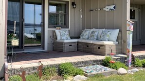 Eine überdachte Veranda mit Sitzgelegenheit, Blick auf das Wasser und ein kleiner Garten.