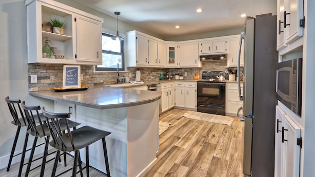 A modern kitchen with white cabinets, a central island with bar stools, a stainless steel refrigerator, and a stone backsplash.
