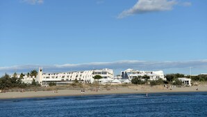 Ein Küstenhotel mit mehreren weißen Gebäuden, einem Strand und blauem Himmel.
