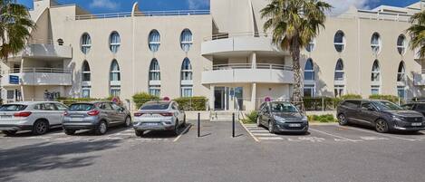 A modern hotel with a parking lot, multiple cars, and a clear blue sky.