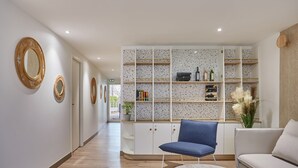 Ein modernes Interieur mit Holzboden, einem blauen Sessel, einem weißen Sofa und einer eingebauten Bücherwand mit Büchern und Dekorationsgegenständen.