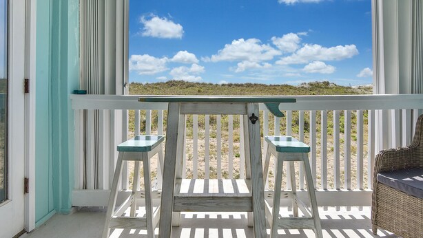 Een balkon met uitzicht op het strand, een rieten stoel en twee krukken.