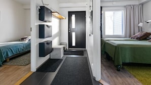 A modern, well-lit room with a bed, a desk, and a chair. There is a window with curtains, a door, and a wall-mounted shelf with decorative items. - Skivillas 78 ukkohalla (2) by Interhome (Hyrynsalmi)