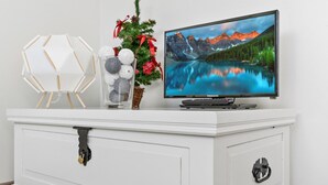 A white entertainment center with a flat-screen TV, a decorative glass vase with white and gray spherical ornaments, and a small Christmas tree with red ribbons and pine cones. - Skivillas 78 ukkohalla (2) by Interhome (Hyrynsalmi)