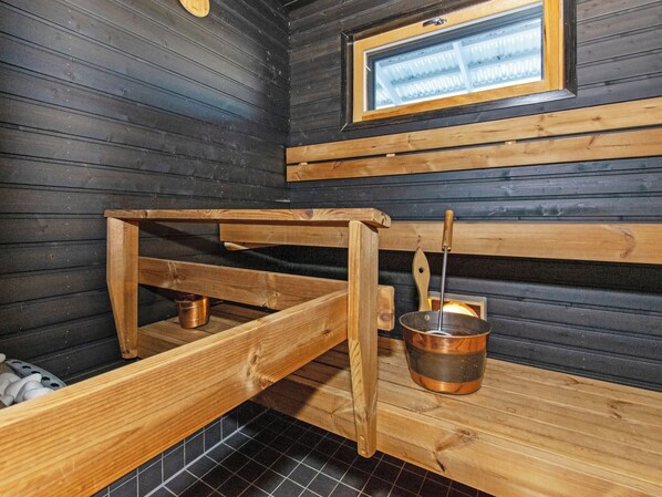 A sauna room with wooden benches, a metal bucket, and a window.
