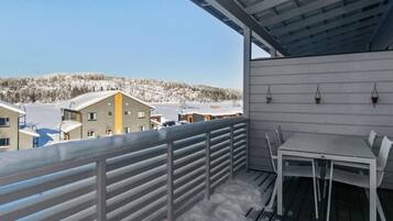 Een balkon met uitzicht op een besneeuwd landschap, een tafel met stoelen en een hekwerk.