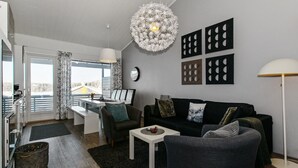 A modern living room with a sofa, armchair, and coffee table. There is a dining area with a table and chairs, and a kitchen area with a stove and sink. - Skivillas 78 ukkohalla (2) by Interhome (Hyrynsalmi)