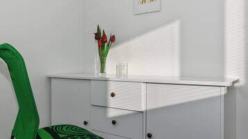Ein Zimmer mit einem weißen Schreibtisch, einem grünen Stuhl, einer Vase mit roten Blumen und einem gerahmten Katzenbild.