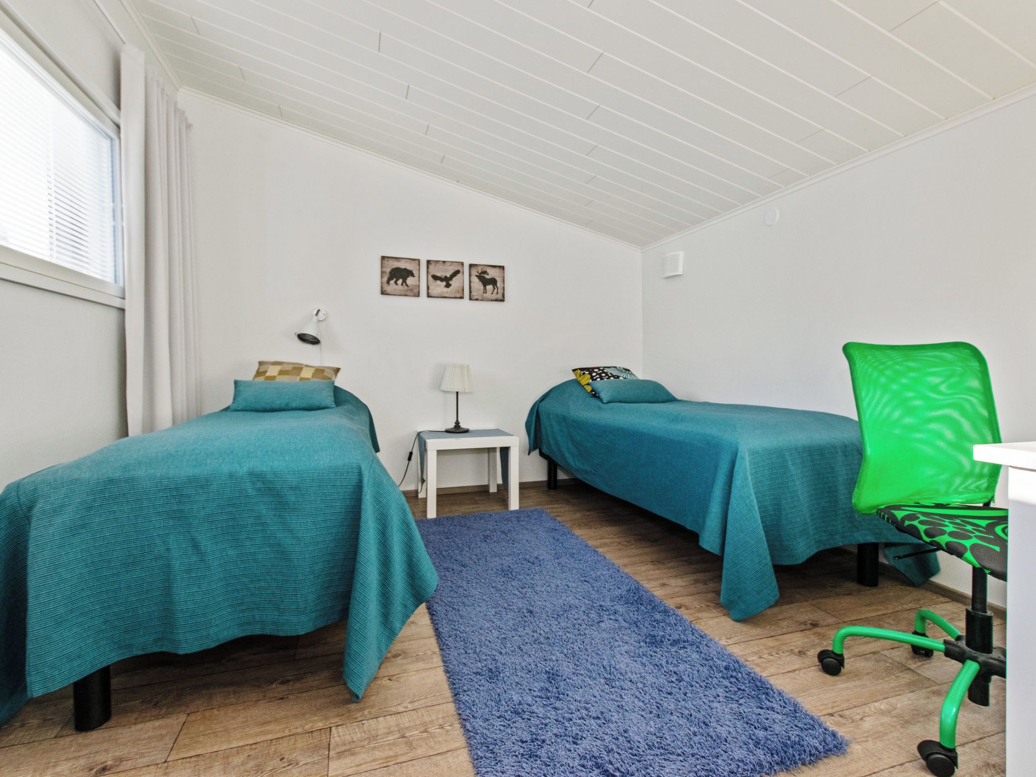 Een kamer met twee eenpersoonsbedden, een bureau met stoel, een klein tafeltje met lamp en een blauw vloerkleed.