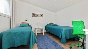 Een kamer met twee eenpersoonsbedden, een bureau met stoel, een klein tafeltje met lamp en een blauw vloerkleed.