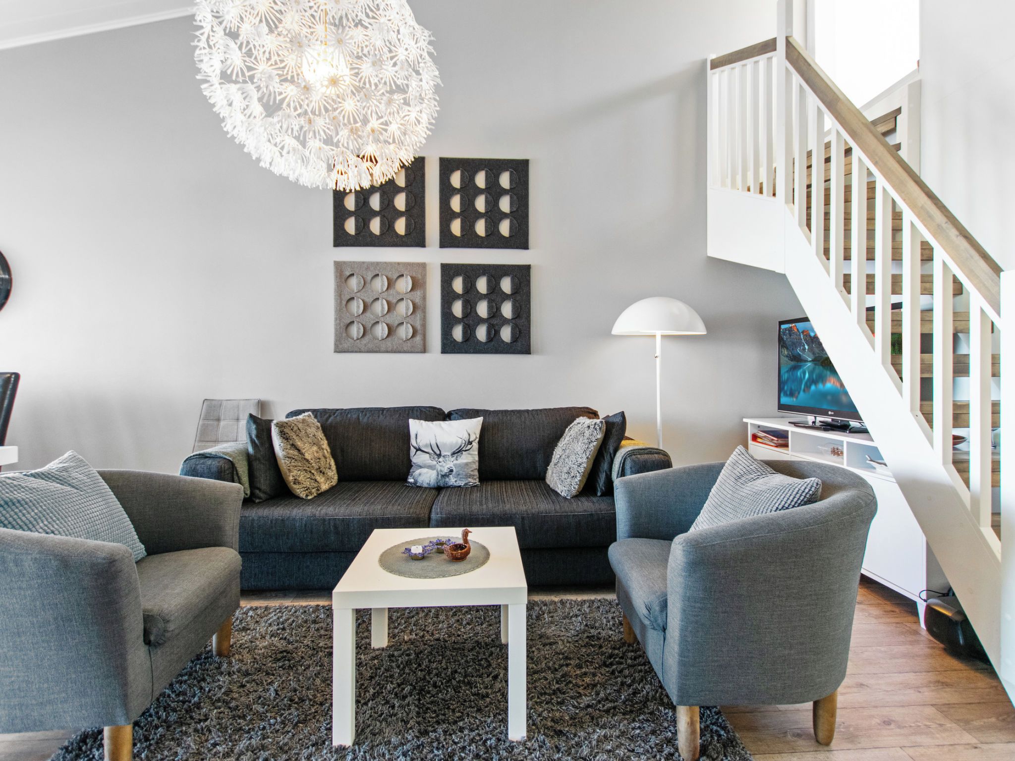 A modern living room with a grey sofa, two armchairs, a coffee table, and a chandelier.