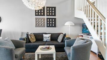 Een moderne woonkamer met een grijze bank, twee fauteuils, een salontafel en een kroonluchter.