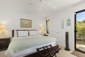 Ett sovrum med en säng, sänglampor, en takfläkt, en dörr som leder ut till en balkong och ett litet bord med en stol.